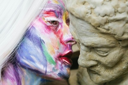 Gros plan d'une femme au visage peint faisant une confidence à l'oreille d'un statue grecque